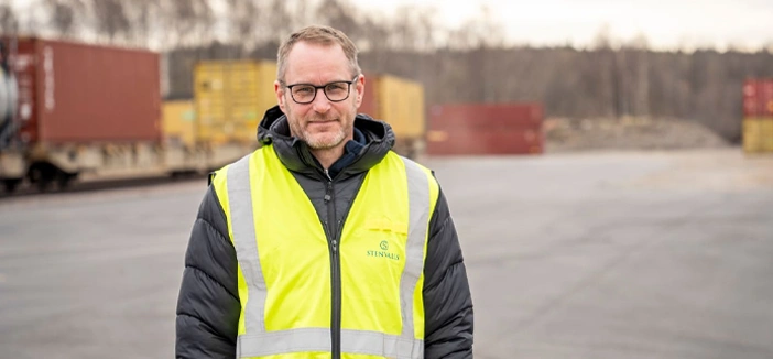 A man in a yellow jacket with containers in the background.