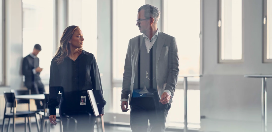 Two people walking through an office complex while chatting.